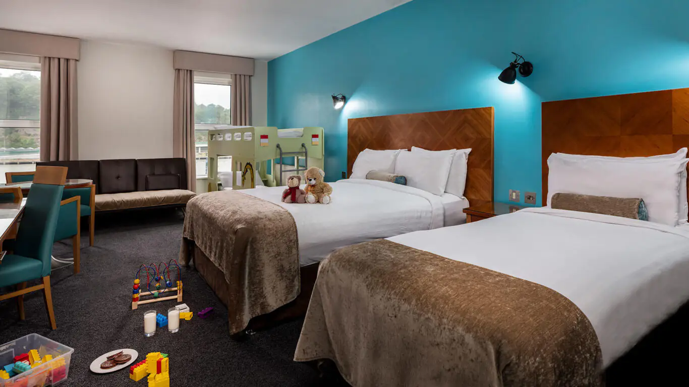 Family-friendly hotel room with two cosy beds, bunk beds, toys, and river views, ideal for a relaxing, fun stay.