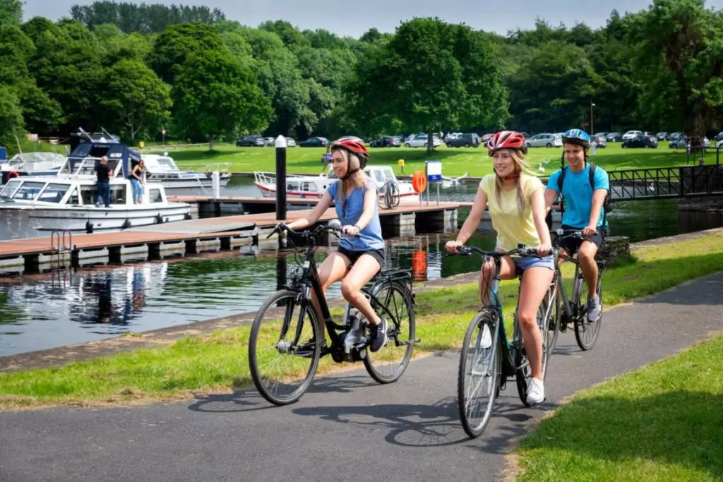 Guests cycling by a scenic lake, with lush greenery and boats, enjoying outdoor activities and tranquil scenery at the hotel.