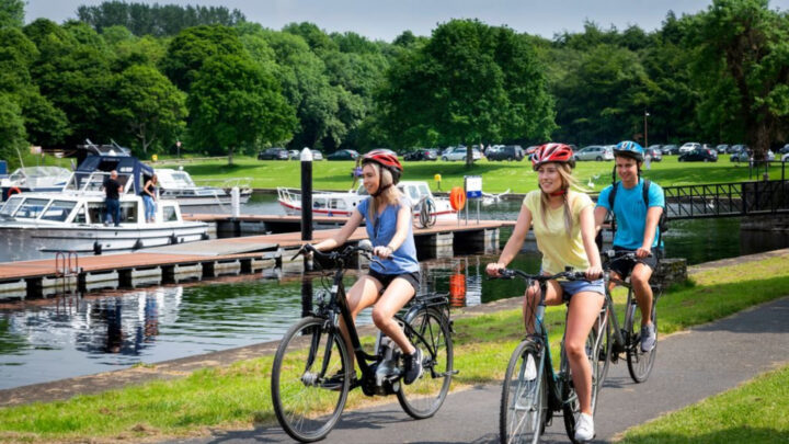 Guests cycling by a scenic lake, with lush greenery and boats, enjoying outdoor activities and tranquil scenery at the hotel.