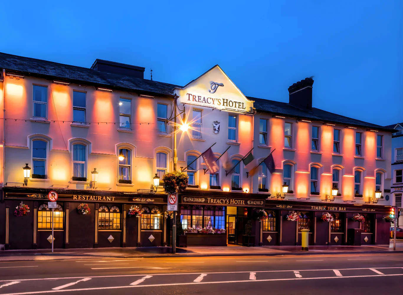 Charming hotel fa&ccedil;ade at dusk, glowing warmly; flags, welcoming light, and inviting entrance to Croker's dining and bar.
