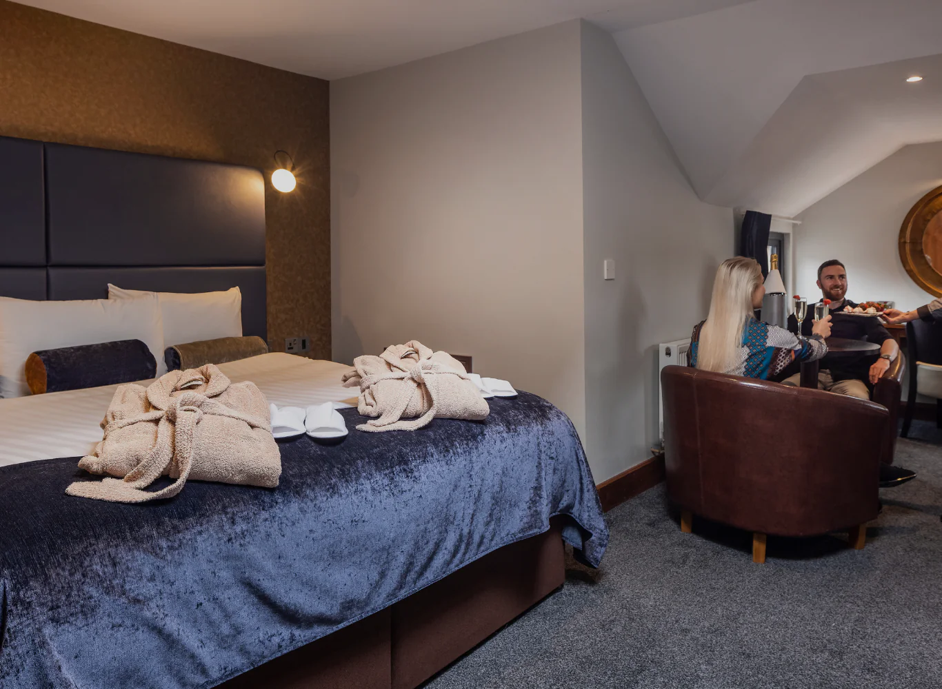 Elegant hotel room with king-size bed, cosy seating area, guests enjoying room service, welcoming atmosphere.