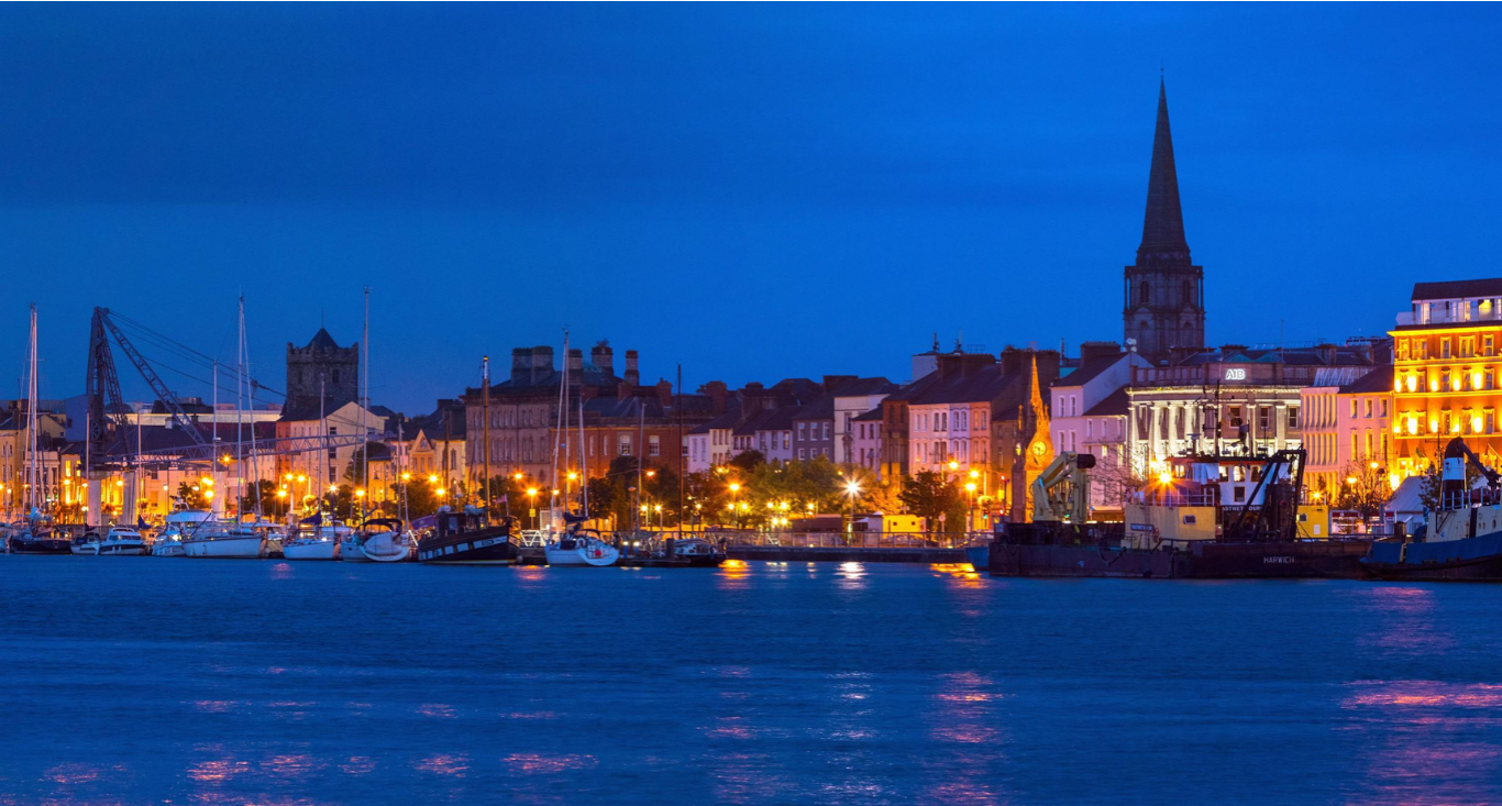 Stunning waterfront view of a vibrant cityscape with historic buildings and boats at dusk, highlighting a welcoming atmosphere.