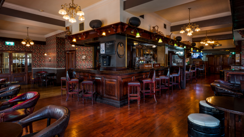 Cosy hotel pub with wooden bar and leather seating, offering a warm atmosphere with vintage d&eacute;cor and elegant chandeliers.