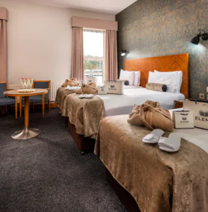 Elegant hotel room with twin beds, chic decor, Elemis toiletries, champagne on table, and window view.