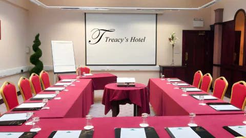 Elegant hotel conference room with red chairs, U-shaped table, presentation screen, perfect for meetings and events.
