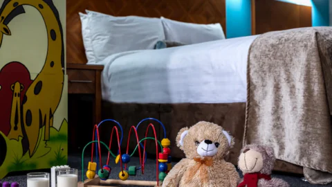 Family-friendly hotel room with cosy bed, playful toys, soft teddy bears, and milk with cookies, creating a welcoming atmosphere.