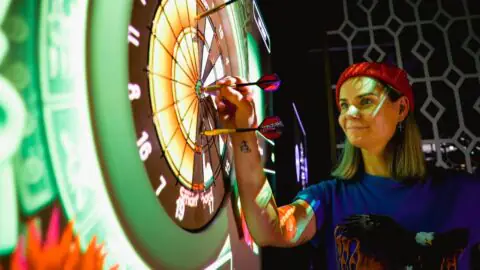 Guest enjoying electronic darts in vibrant hotel game room, featuring interactive entertainment and modern d&eacute;cor.