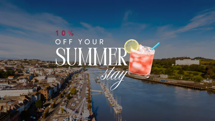 Charming riverside town view with summer drink and 10% off stay offer. Perfect for a relaxing holiday getaway.