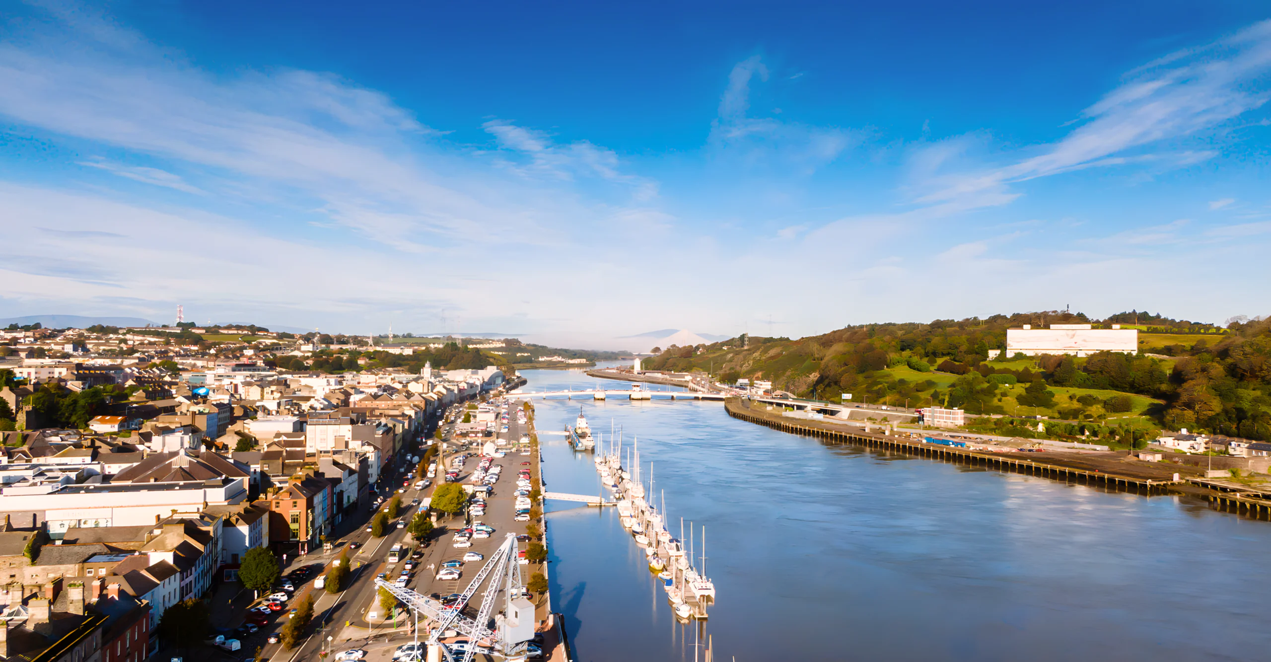 Scenic river view with moored boats, charming town buildings, and lush greenery under clear skies, ideal for a relaxing getaway.