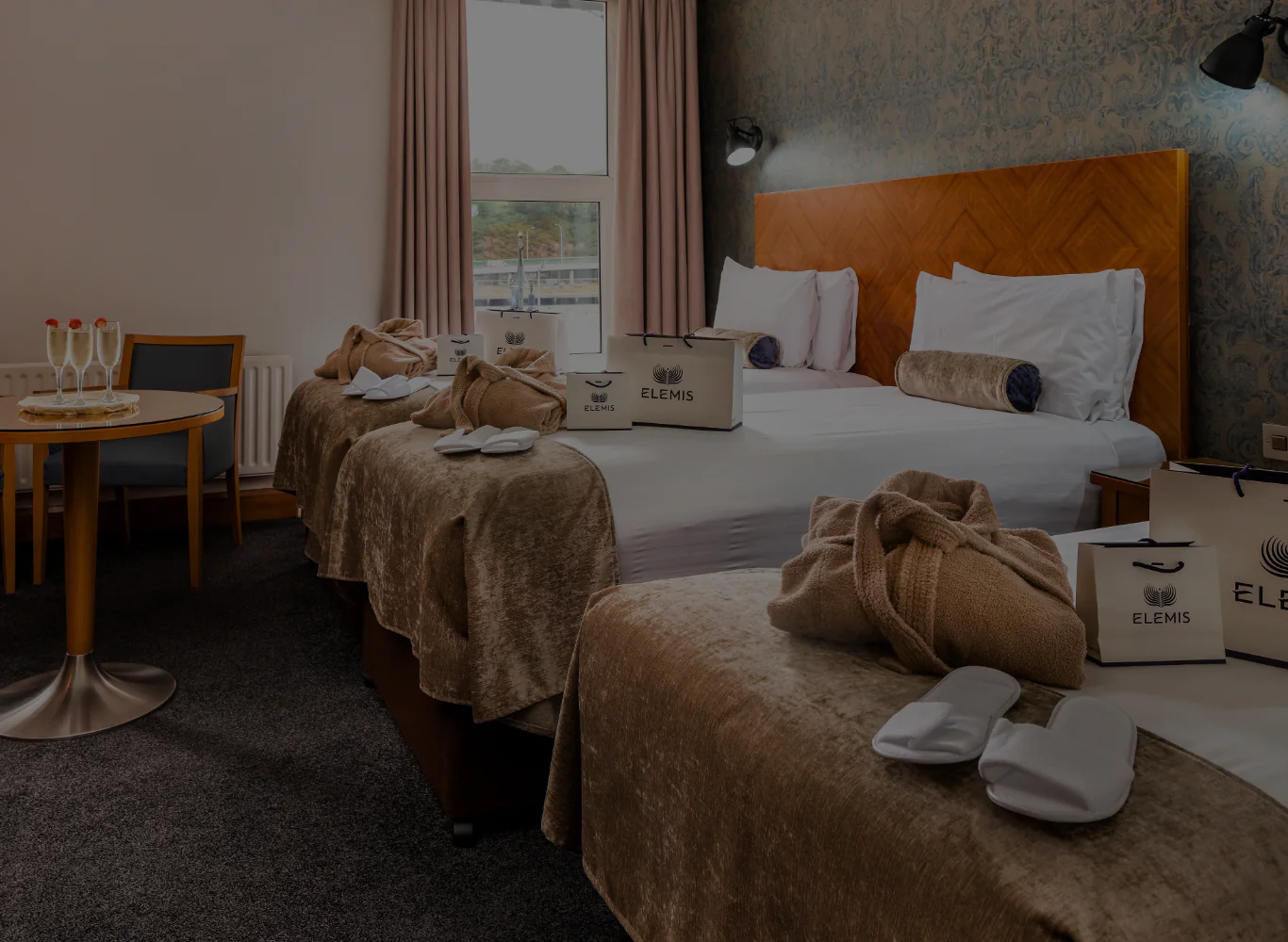 Spacious hotel room with twin beds, plush robes, Elemis toiletries, and a quaint seating area. Perfect for luxury city breaks.