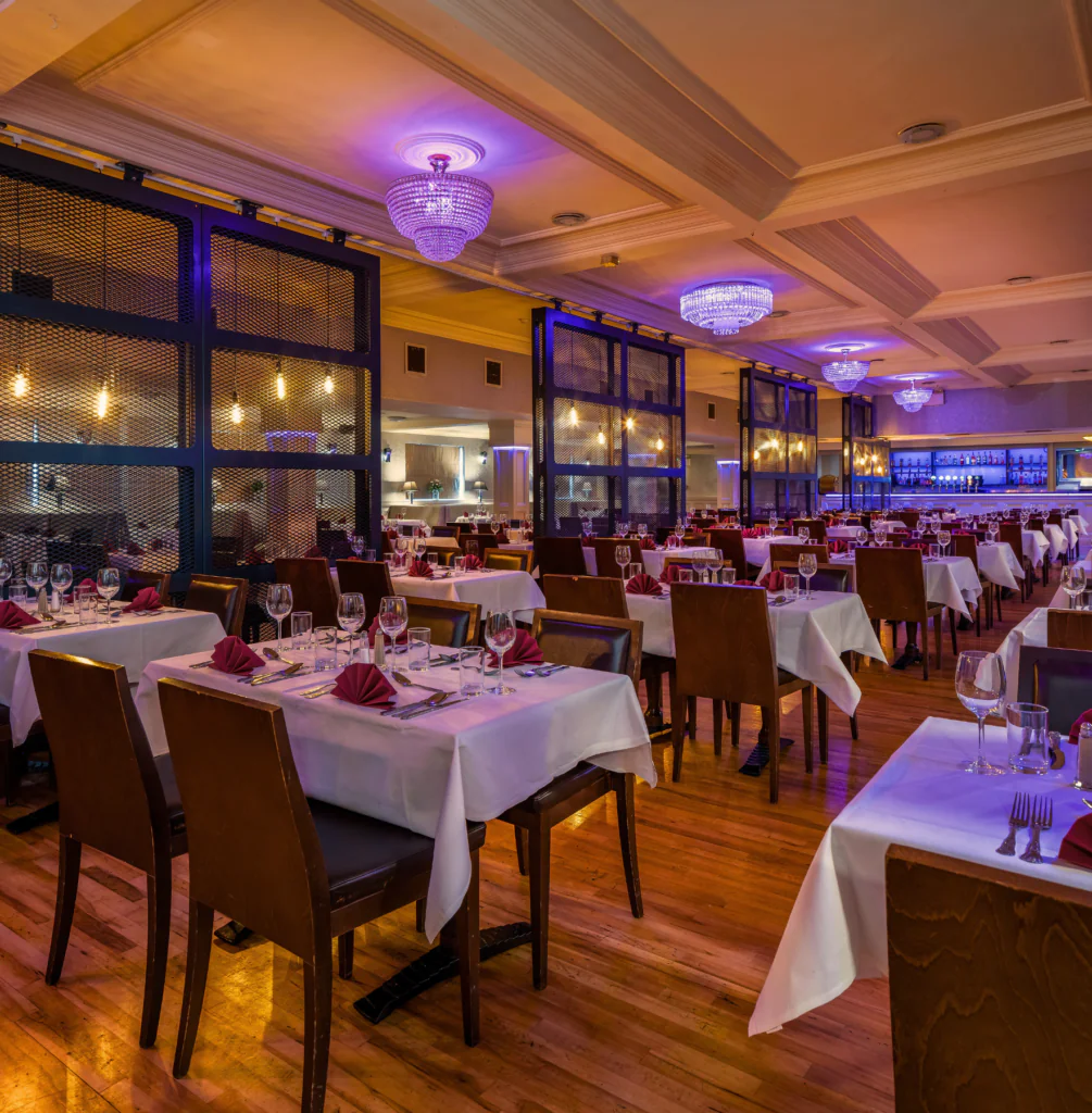 Elegant hotel restaurant with chandeliers, ambient lighting, neatly set tables, promising a warm dining experience.