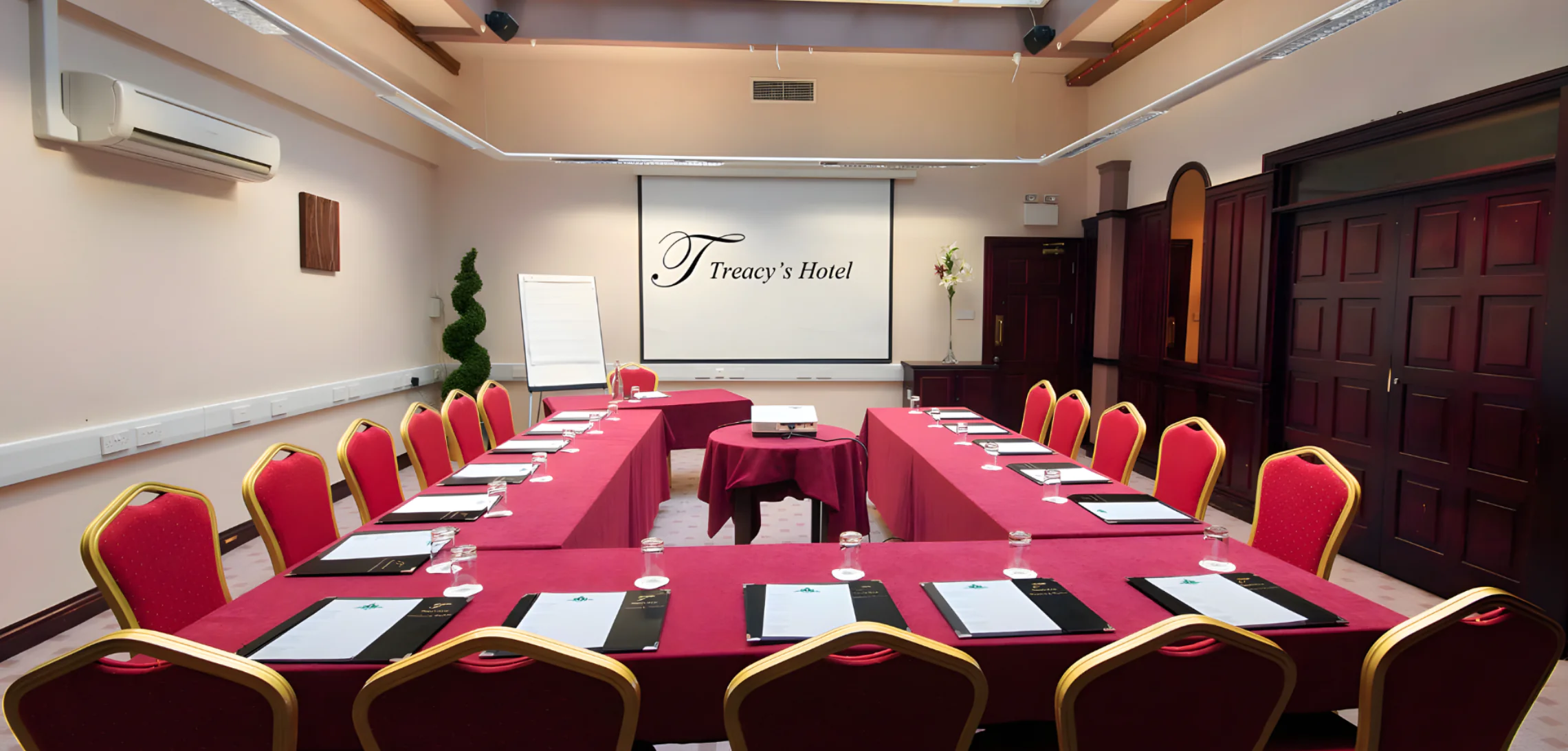 Elegant conference room with U-shaped table, red chairs, projector screen, and professional stationery at luxury hotel.
