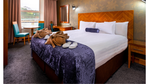 Elegant hotel room with a plush king-sized bed, complimentary robes, slippers, and a window view with cosy seating.