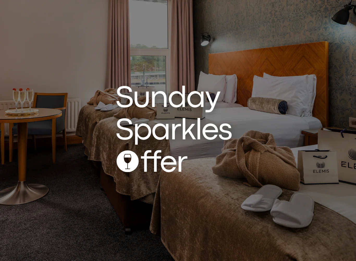 Spacious hotel room with twin beds, soft lighting, gift bags, champagne, and city view, perfect for a relaxing stay.