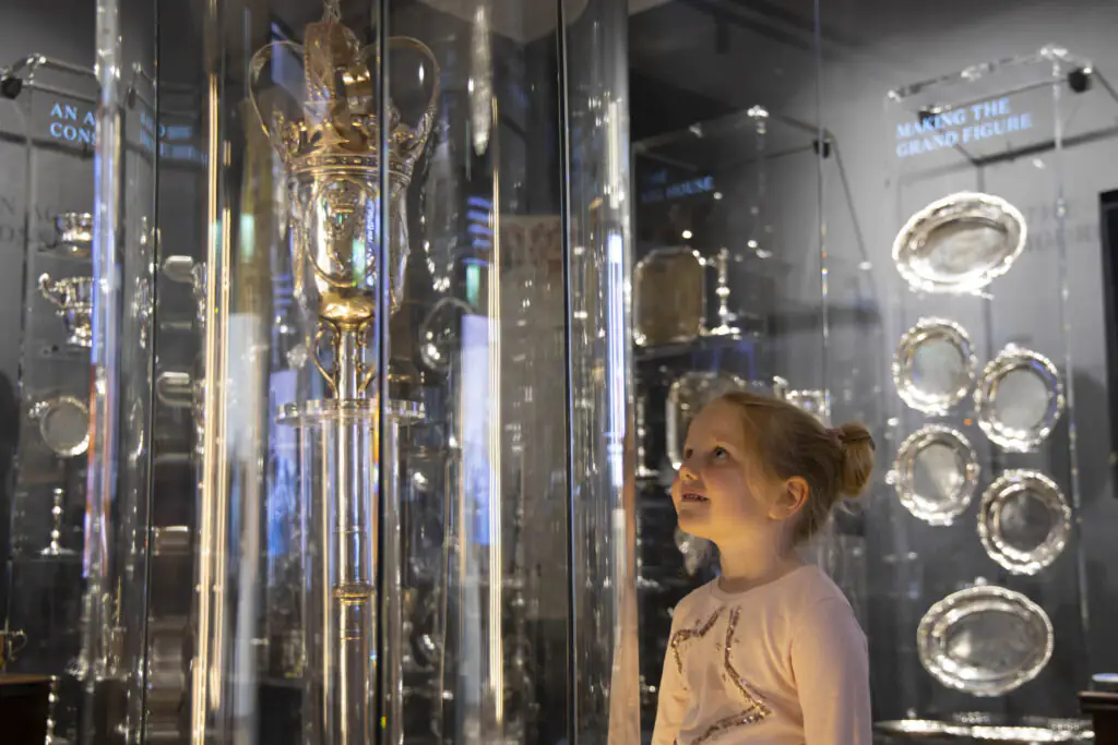 Medieval Museum Child admiring royal silver artefacts in display case at hotel, highlighting cultural elegance and luxury amenities.