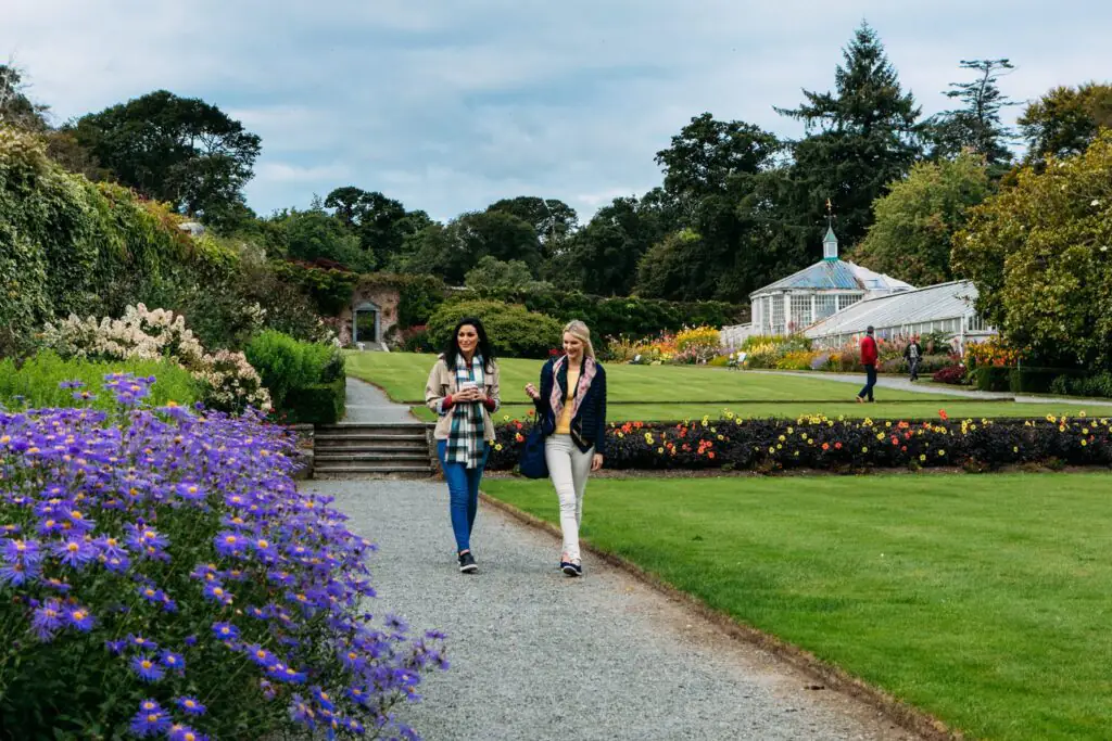 Mount Congreve Gardens Waterford Guests enjoy a stroll through lush gardens and vibrant flowers near a glass conservatory at a countryside hotel.