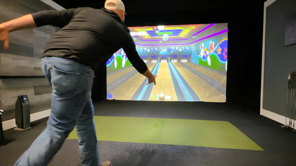 Guest enjoys virtual bowling in hotel's entertainment suite with vibrant graphics and ambient lighting.