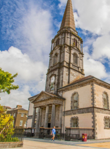 Charming historic church with clock tower under blue skies, near hotel; ideal for exploring local culture and architecture.