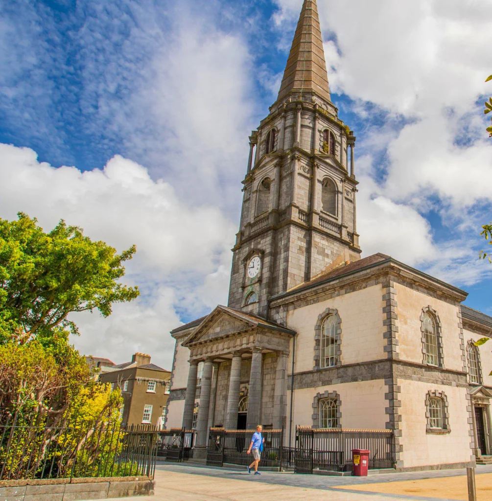 Christ Church Waterford Historic stone church with tall spire, clock, and lush garden; perfect for exploring culture near our welcoming hotel.