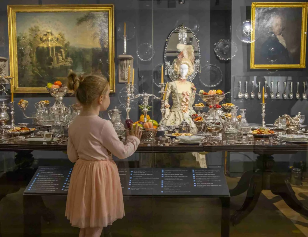 Irish Silver Museum Child admires elegant historical dining display with ornate silverware and period artwork in luxurious hotel gallery.